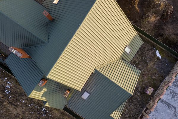 Aerial view of new residential house cottage with shingle roof on fenced yard on sunny day.