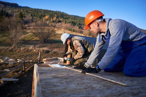 Male builder doing thermal insulation on roof of wooden frame house. Man worker spraying polyurethane foam on rooftop of future cottage. Construction and insulation concept.